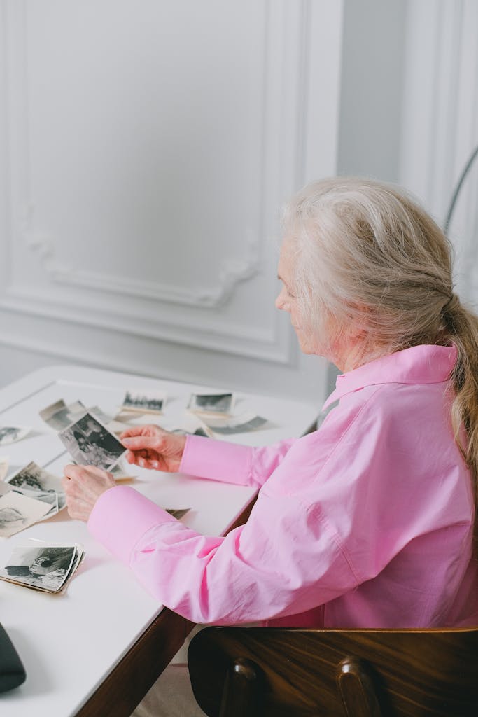 An elderly woman in pink reviews black and white photos, evoking nostalgia.