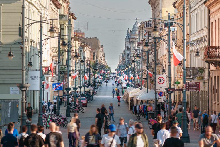 Busy scene on Piotrkowska Street, Ł&oacute;dź with flags and people walking. A vibrant cityscape showcasing Polish culture.